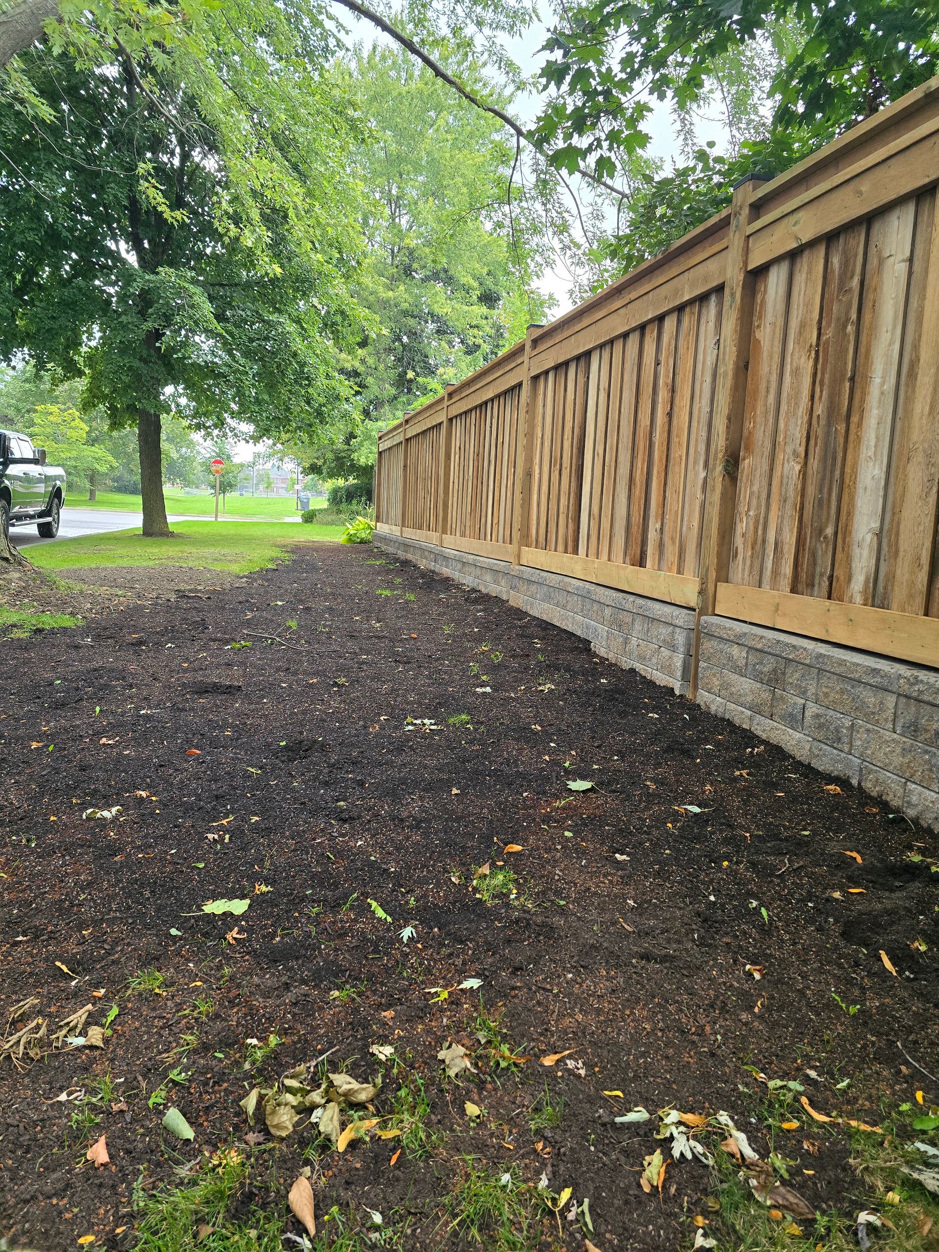 A freshly mulched garden bed alongside a wooden fence. Overcast day.