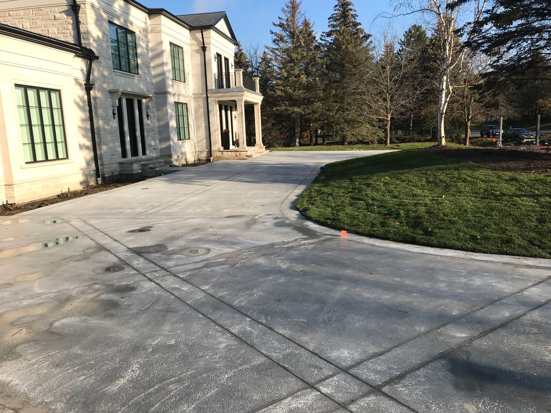 Driveway leading to a two-story beige house with a curved grass patch.