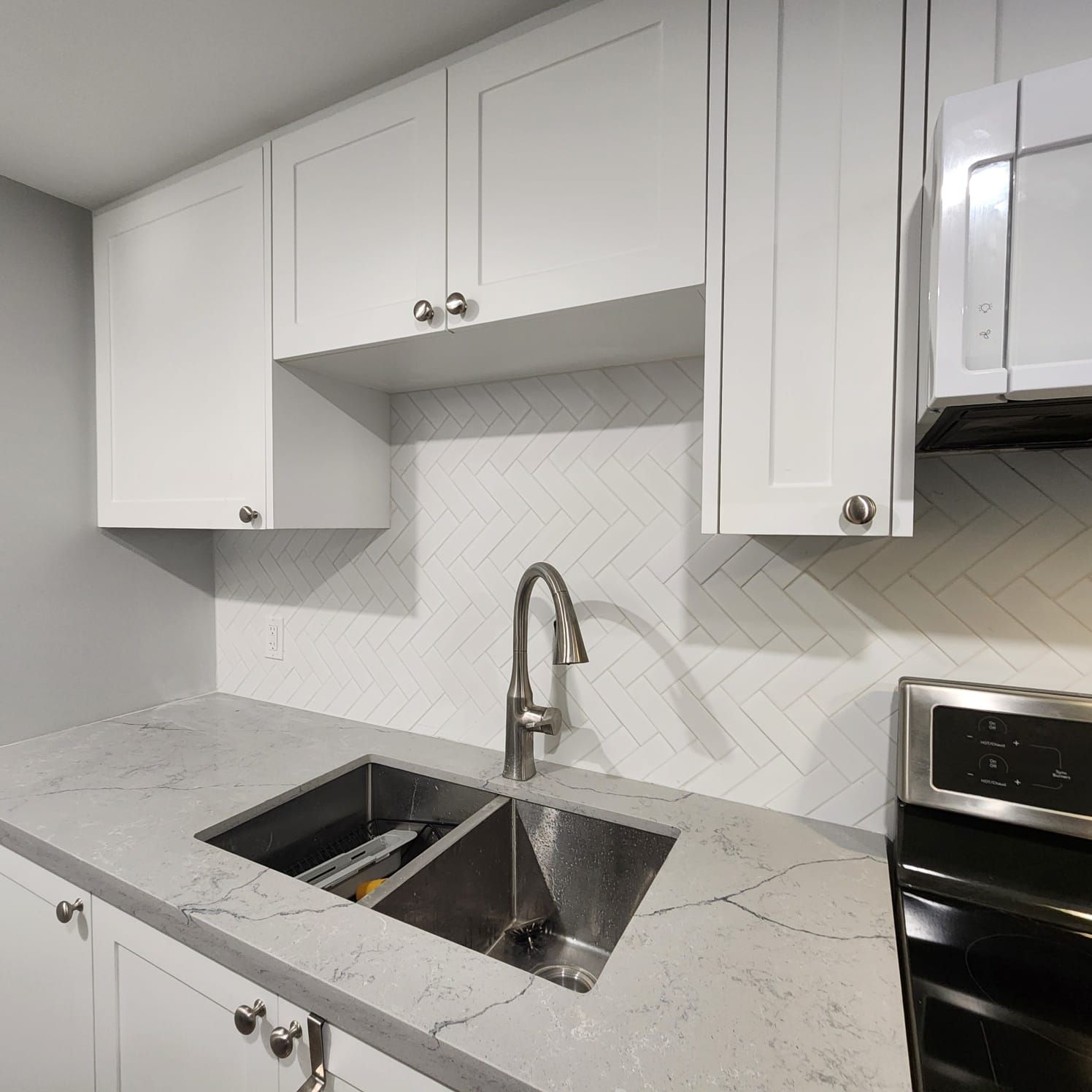 White kitchen with cabinets, stainless steel sink, gray countertop, and white backsplash.