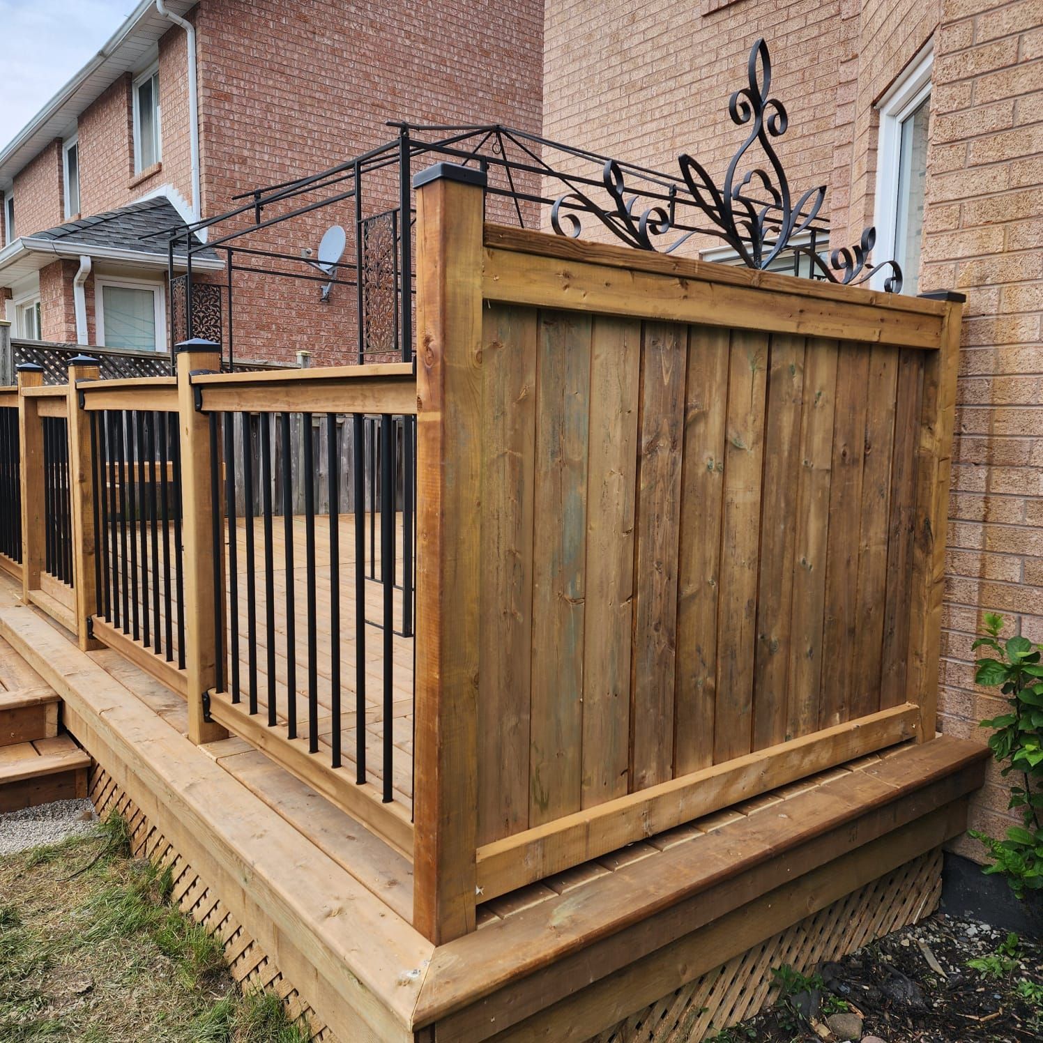 Wooden deck with black railing and vertical wooden privacy fence next to a brick building.