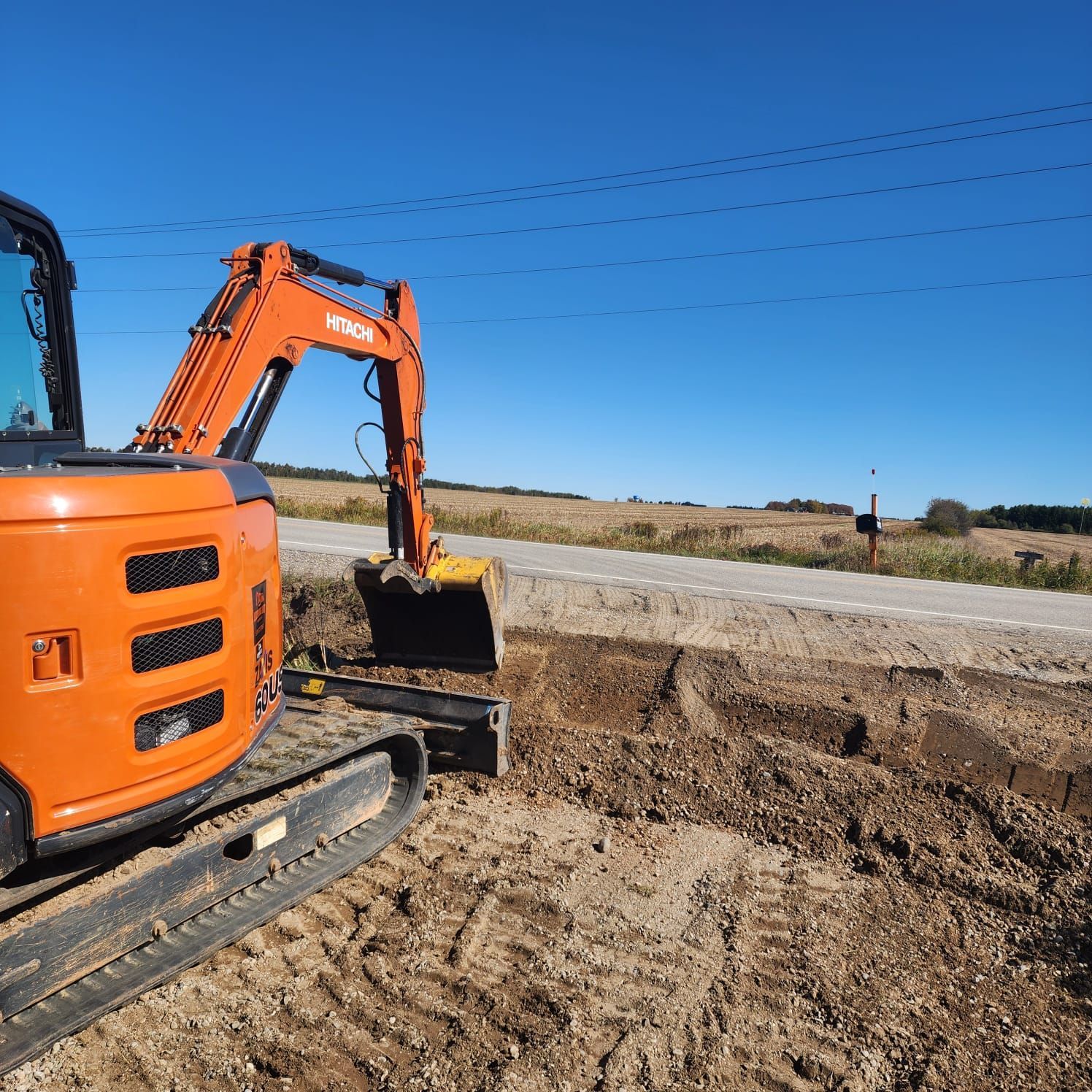 Orange excavator digging alongside a gravel road under a blue sky.