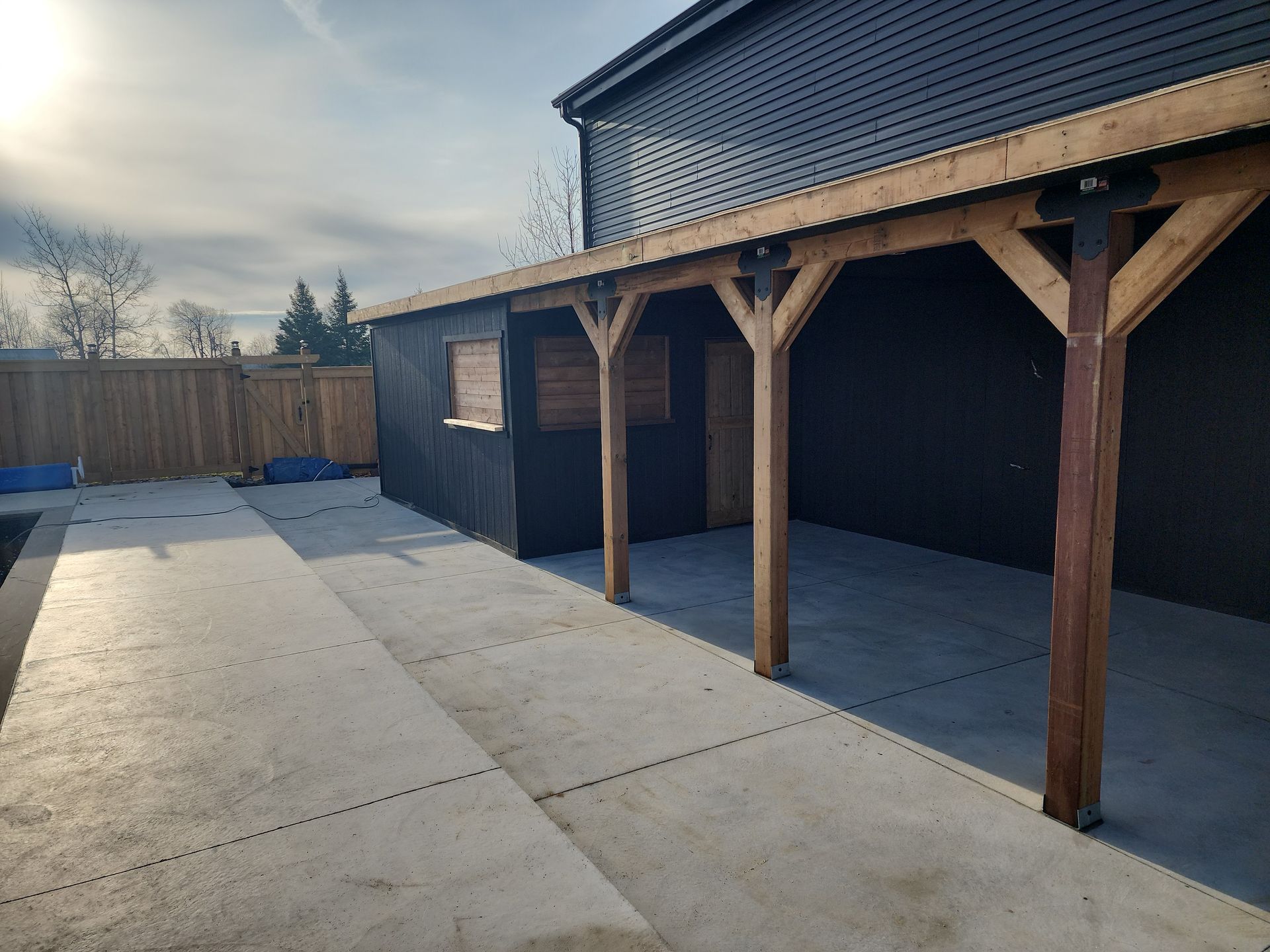 A concrete driveway leading to a black building with a wooden roof