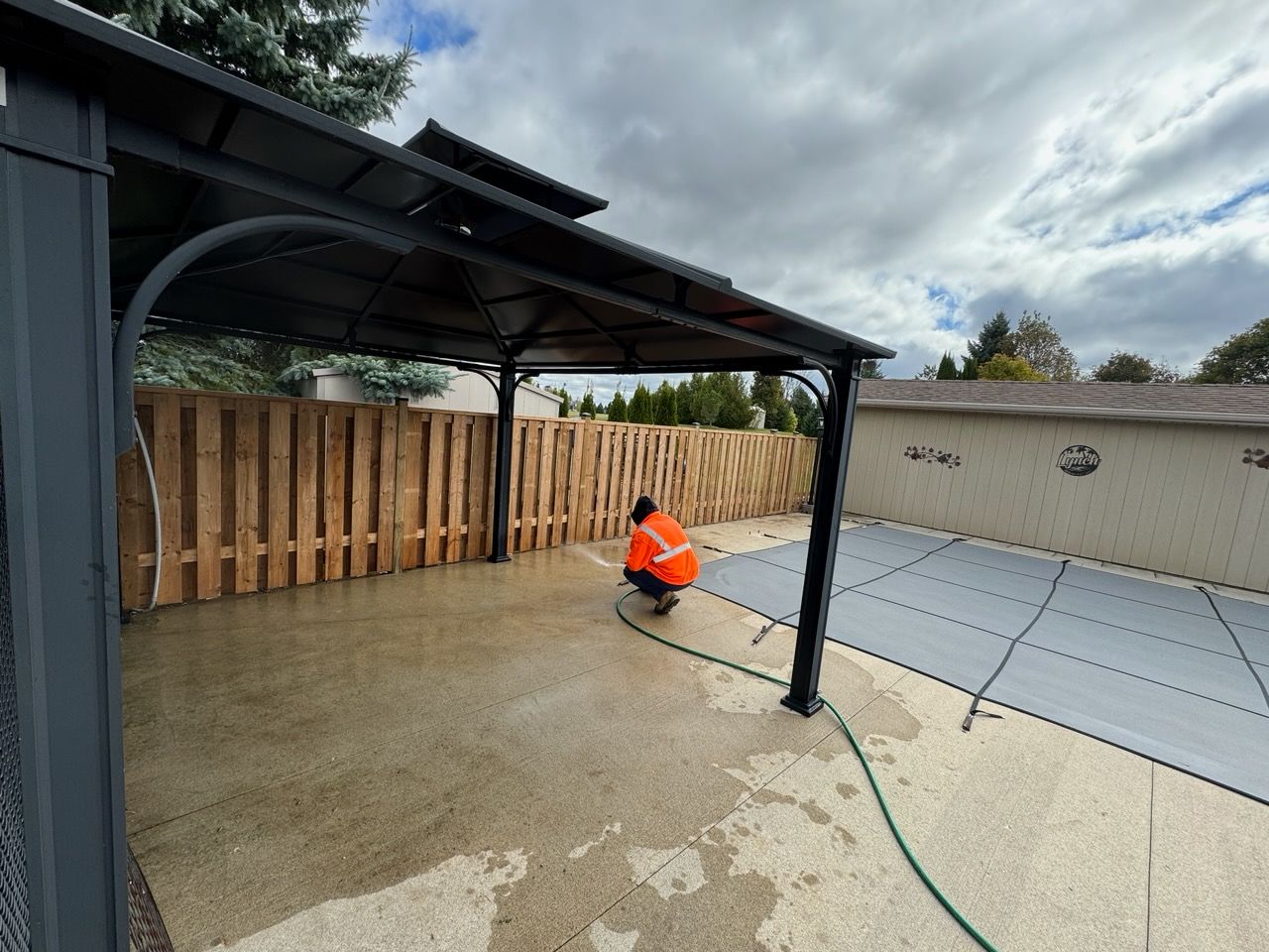 A man is kneeling under a gazebo next to a pool.
