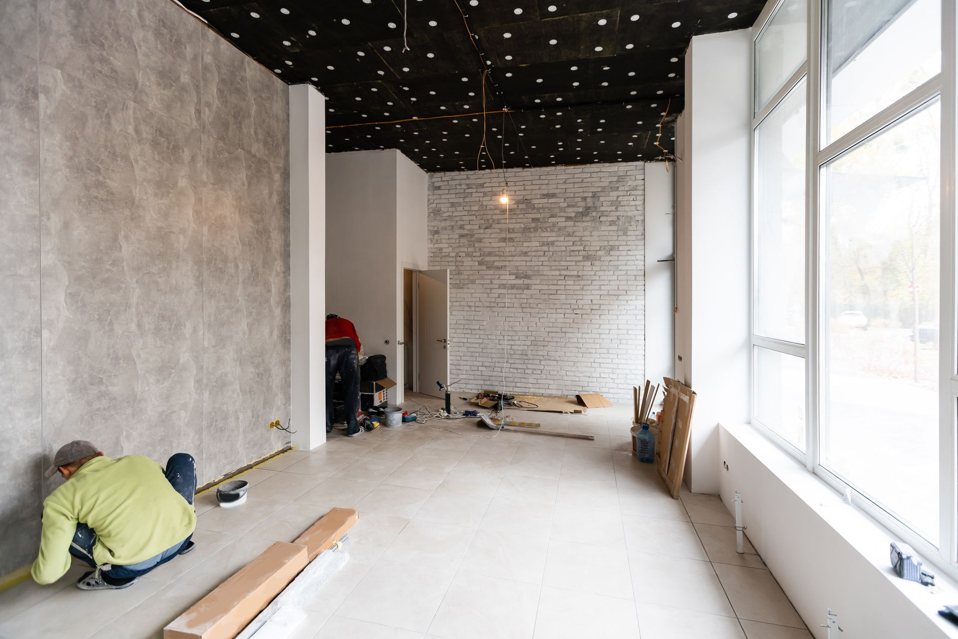 A man is measuring a wall in an empty room.