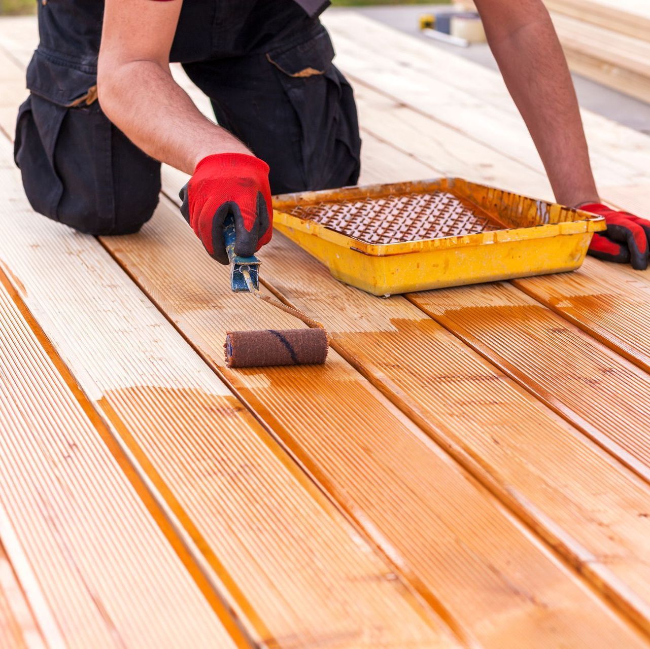 A man is painting a wooden deck with a roller