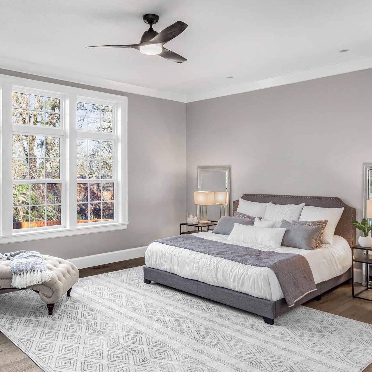 A bedroom with a king size bed , ceiling fan , and lots of windows.