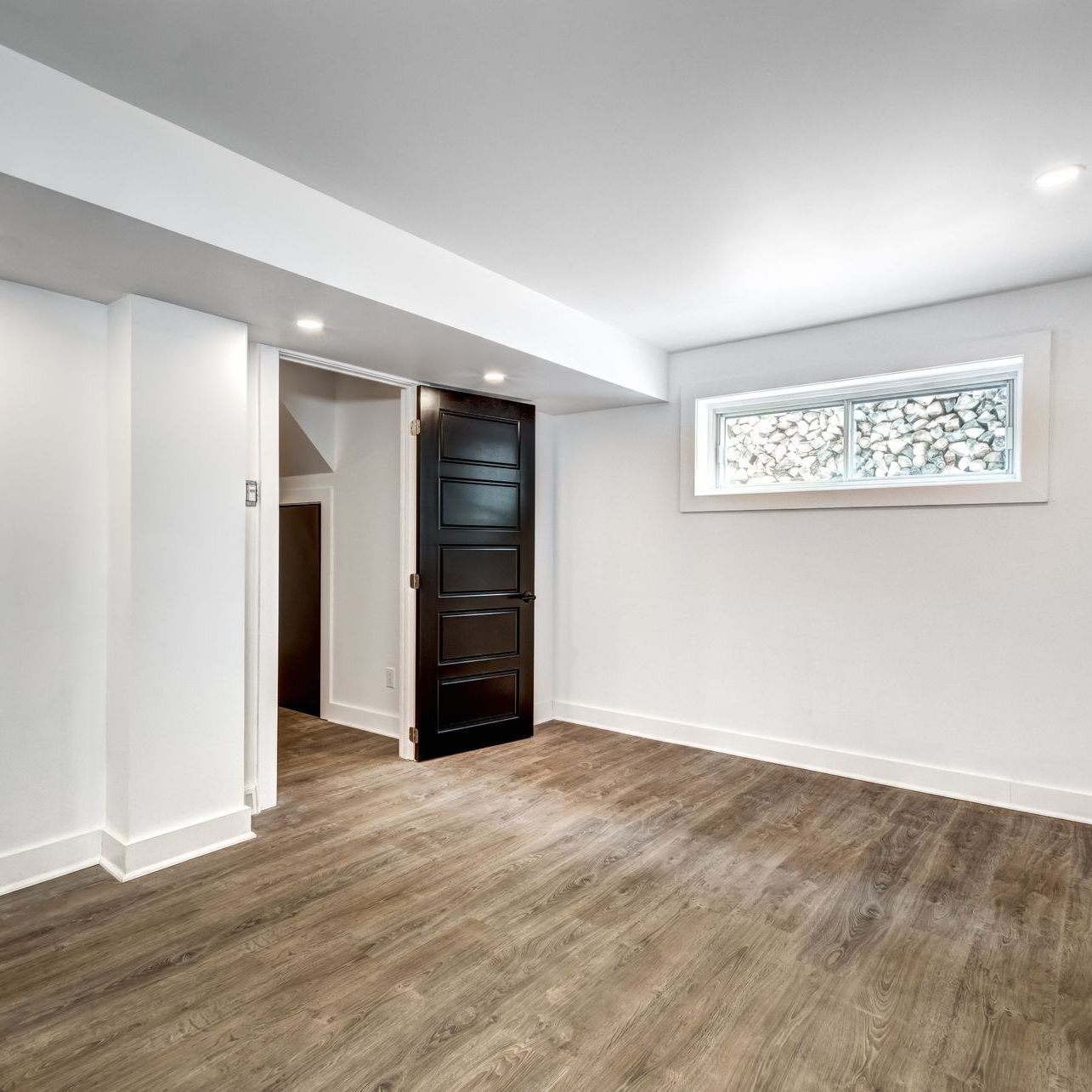 An empty basement with a black door and a window.