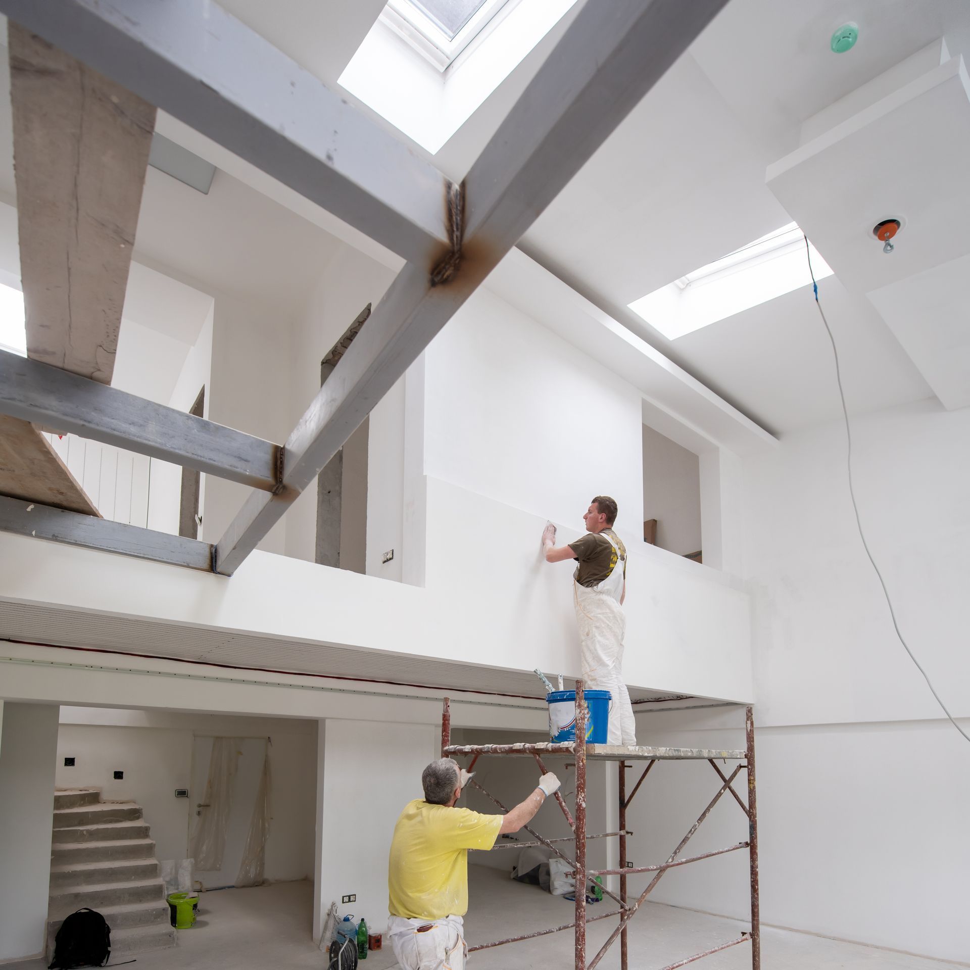 A man standing on a scaffolding painting a wall