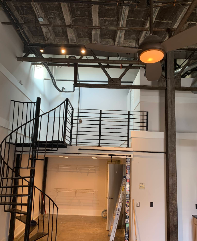 Interior shot of a loft with a spiral staircase, white walls, and exposed beams.