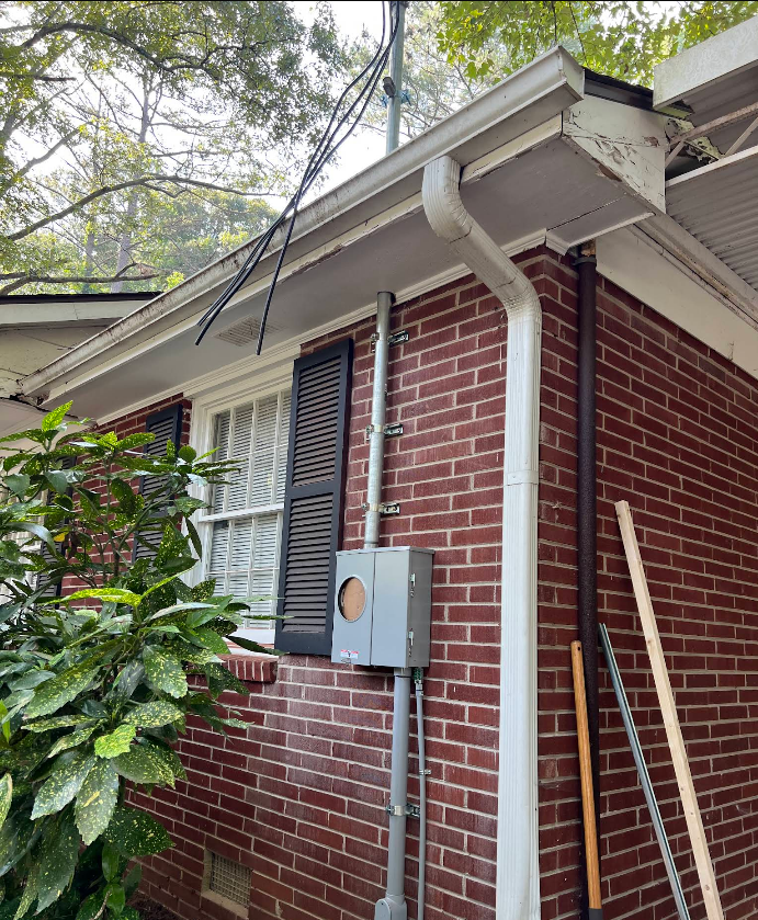 Brick building exterior with gray electrical box, white gutters, black shutters, and power lines.