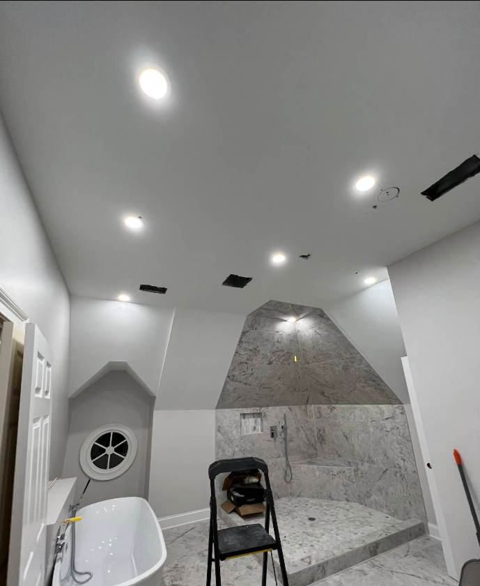 Bathroom remodel in progress. White walls, recessed lighting, gray marble shower, and a black step stool.