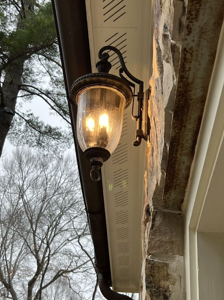 Ornate outdoor lamp on a stone wall, illuminating a cloudy sky, next to a brown gutter.