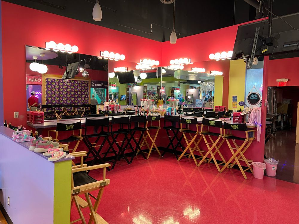 Makeup studio with red walls, mirrors, black director's chairs, and vibrant pink floor.