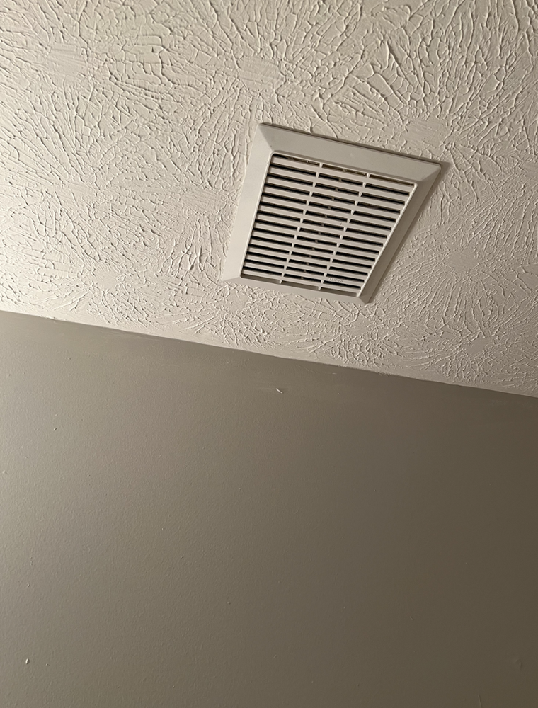 White ceiling vent on textured ceiling above a gray wall.