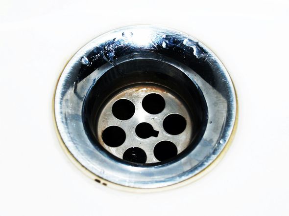A chrome sink drain with a multi-hole metal grate set into a white basin.