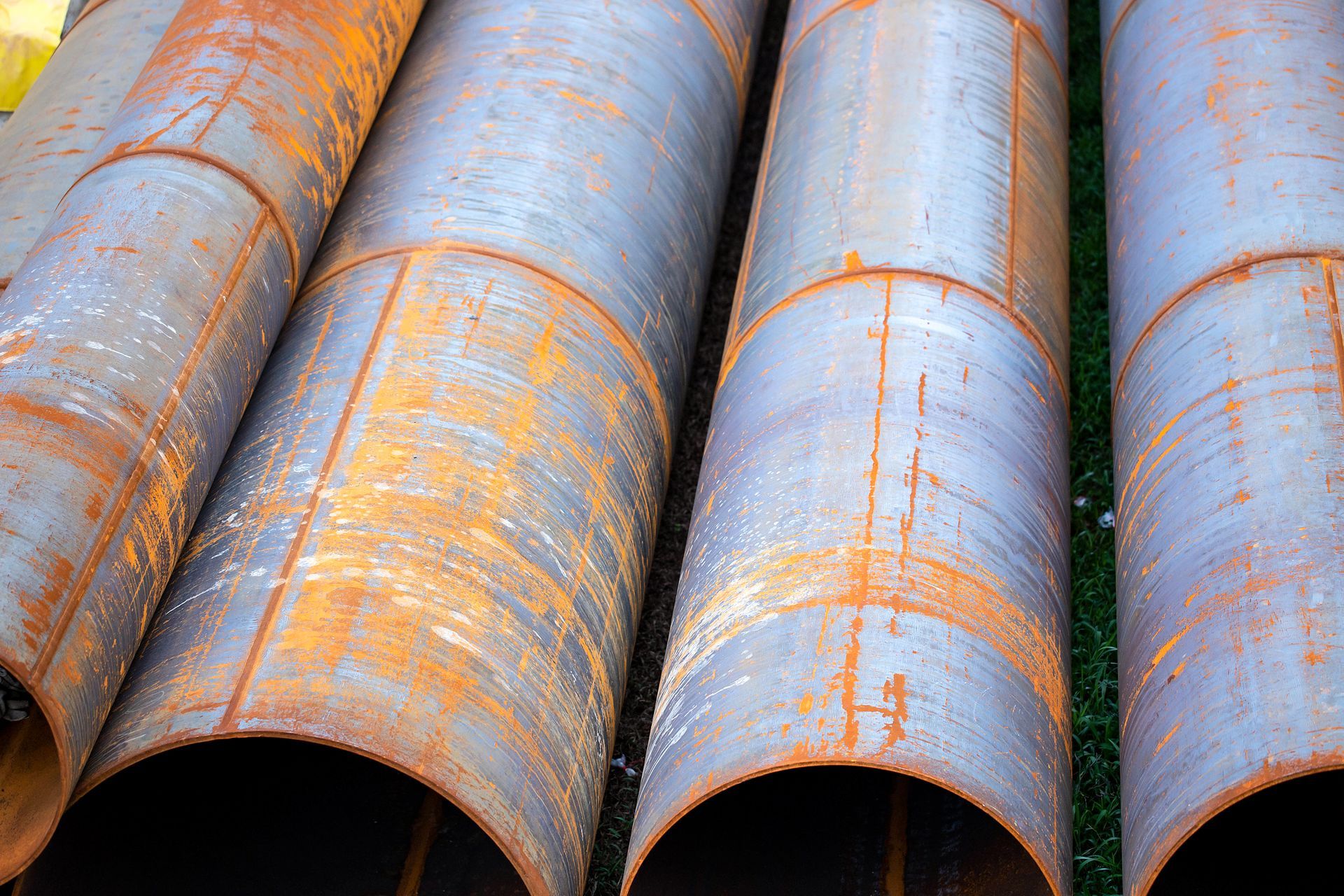 A group of large, industrial steel pipes laying side-by-side with visible patches of rust.