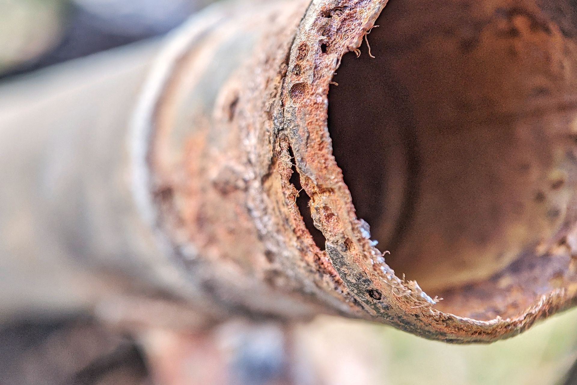 A close-up of a corroded, rusted metal pipe showing severe degradation and flaking metal at the open end.