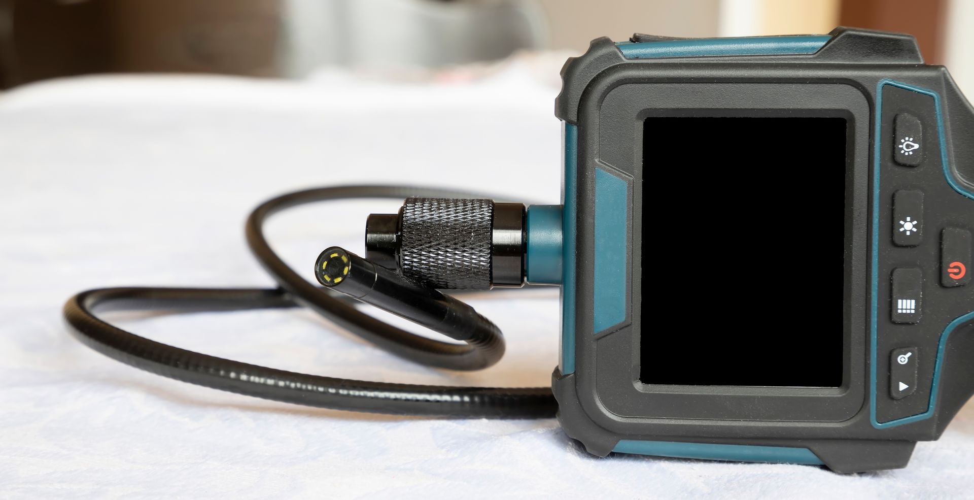 Black action camera with cable and strap on a white surface, screen off