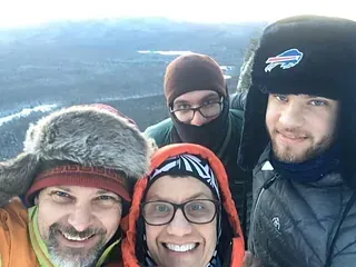Four smiling hikers in winter hats on a snowy mountain overlook
