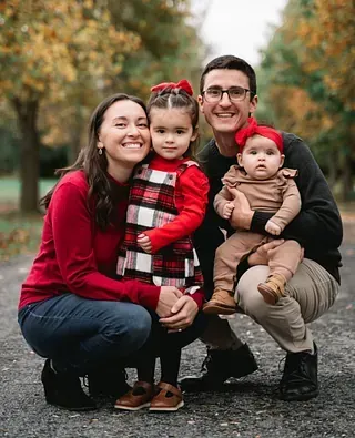 Family of four posing outdoors in autumn, wearing red and brown outfits, smiling at the camera.