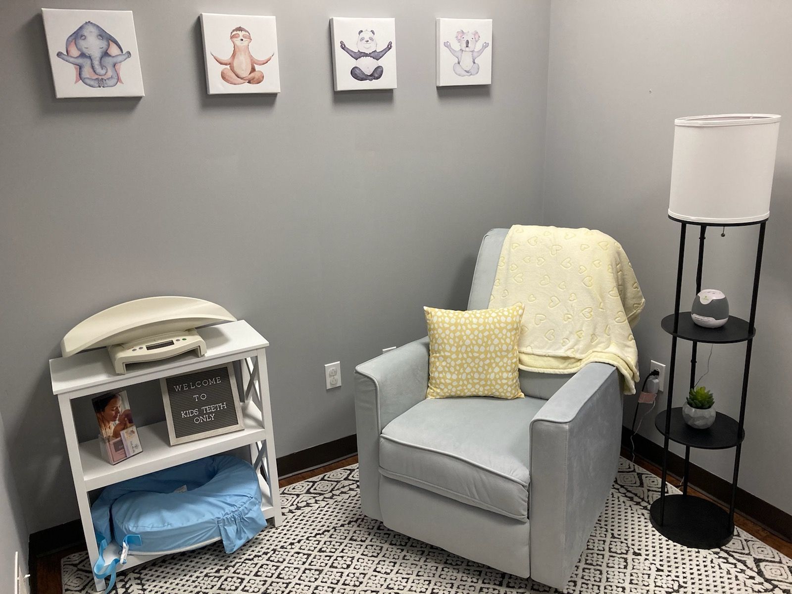 Cozy gray nursery corner with armchair, changing table, floor lamp, and wall art.