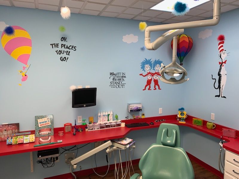 Colorful pediatric dental exam room with chair, overhead lamp, sink, and cartoon wall murals