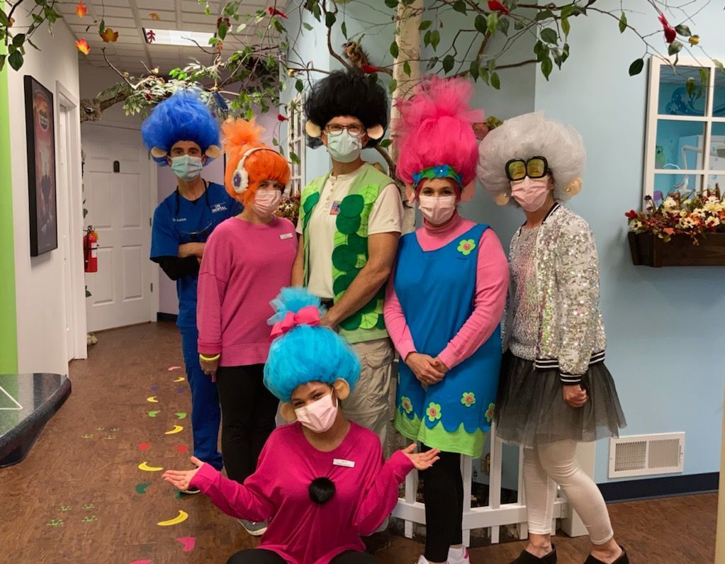 Six people in colorful wigs and costumes posing indoors with confetti on the floor.