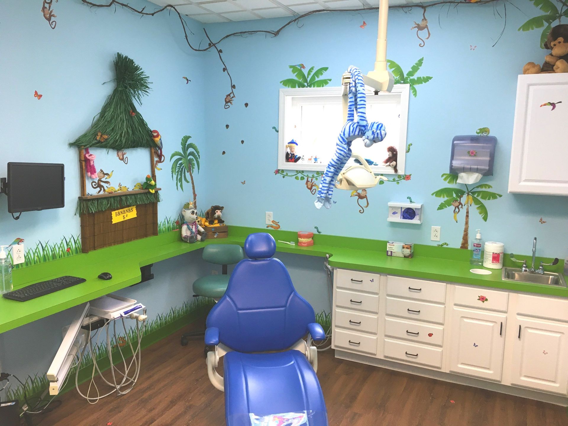 Blue dental exam room with chair, cabinets, sink, and wall-mounted monitors