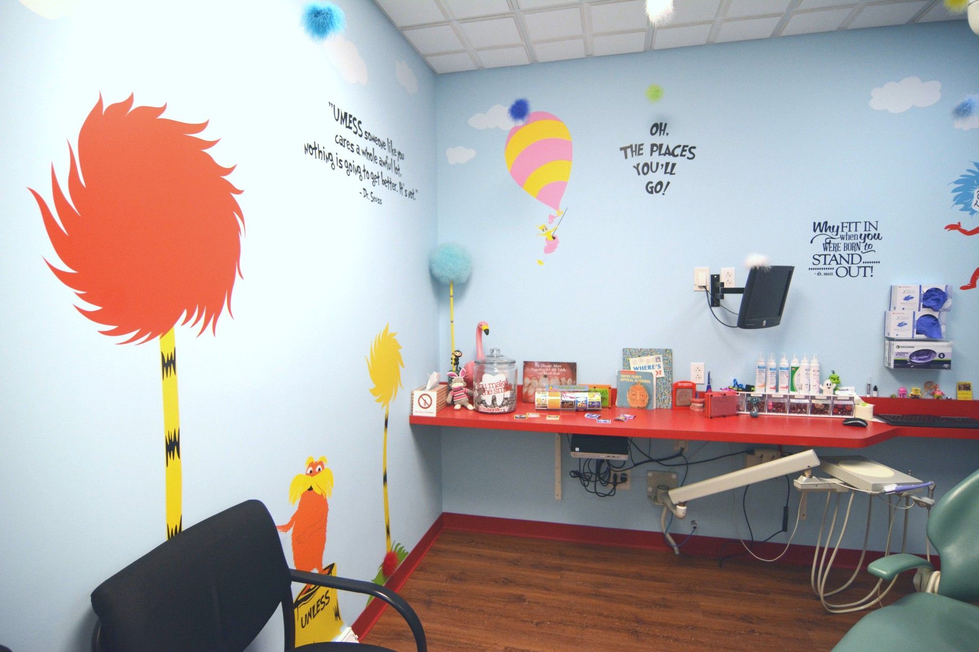 Brightly decorated classroom with desks, colorful wall art, and a red supply table