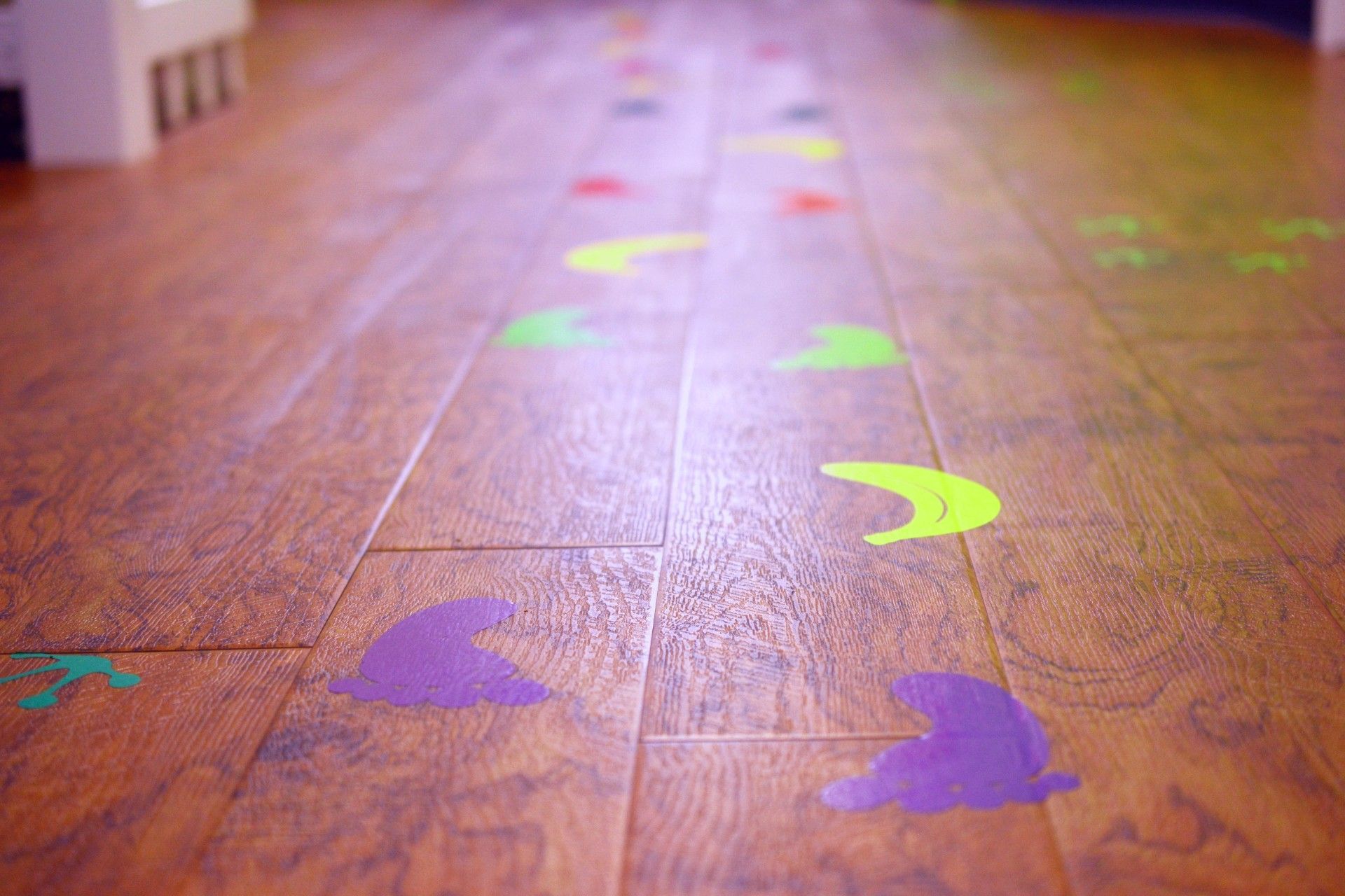 Colorful stencil footprints and shapes scattered across a wooden floor, fading into the distance