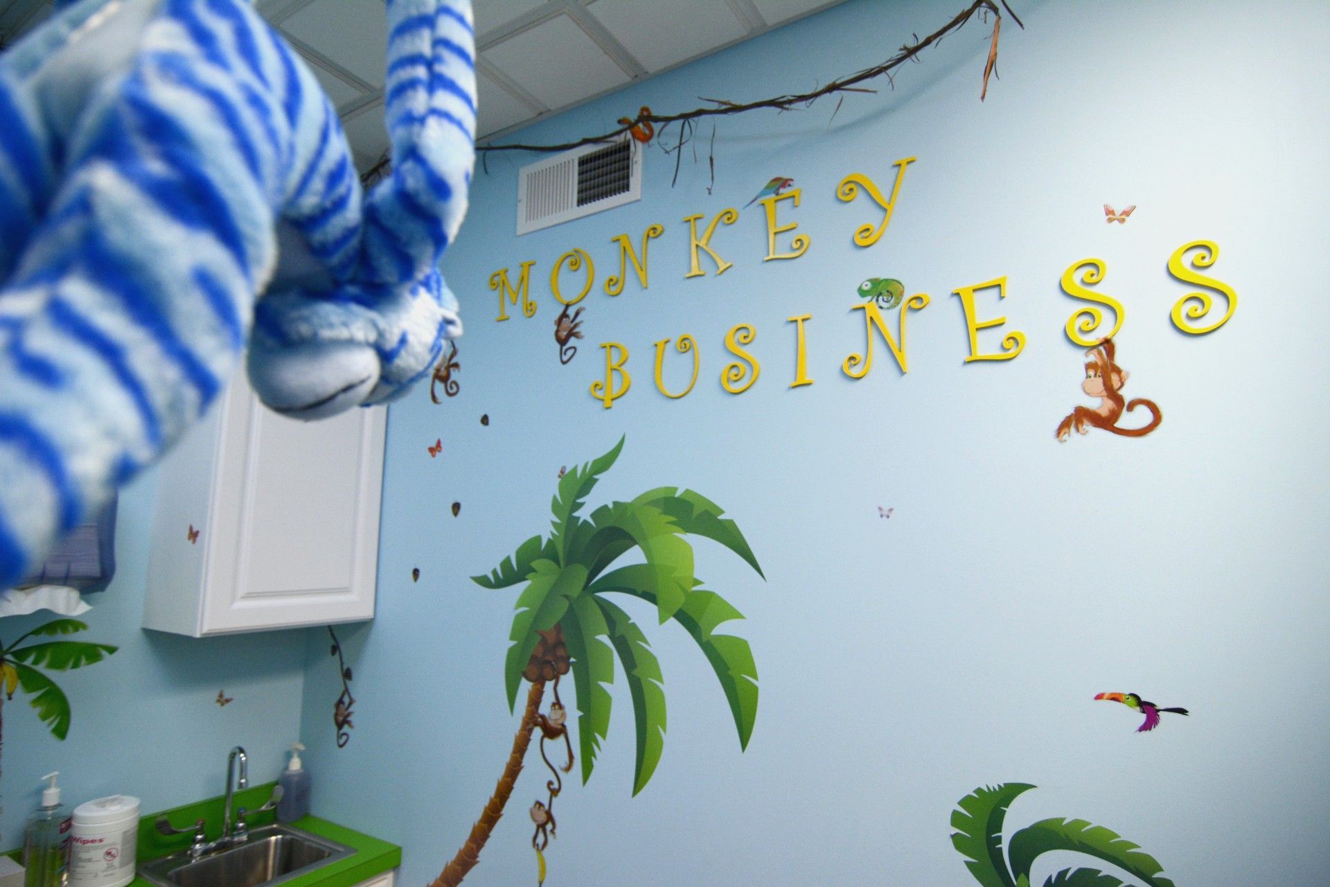 Blue-striped stuffed monkey in a child’s room with “Monkey Business” wall art and palm tree decals