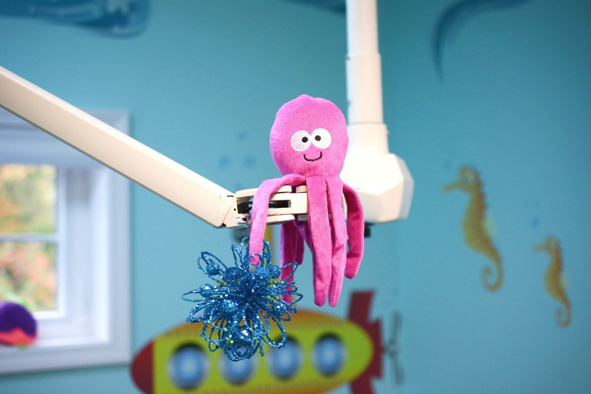 Pink stuffed monkey hanging from a white bar with blue tinsel in a colorful room