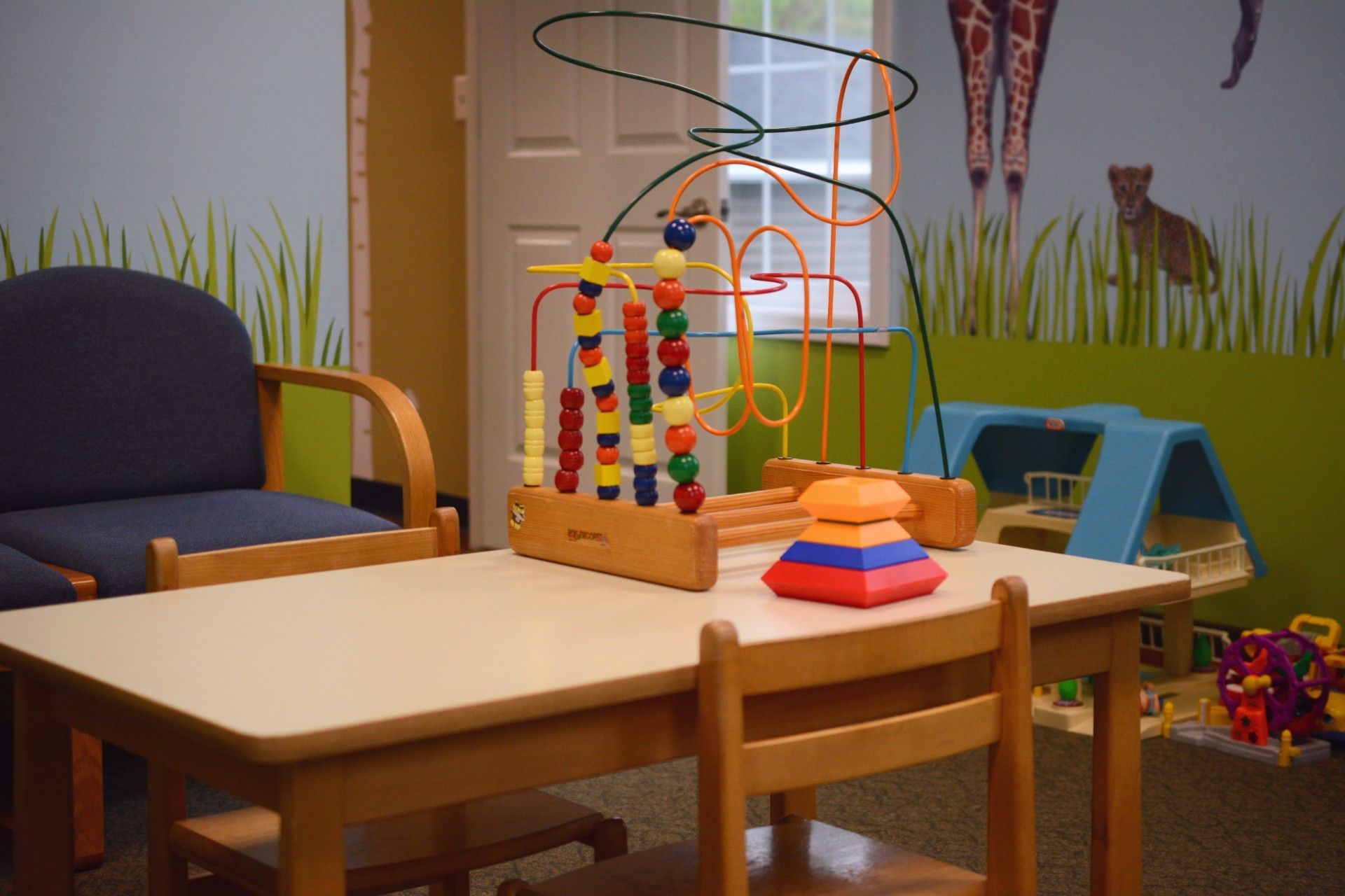 Child’s playroom with wooden tables, colorful bead maze toys, and a blue chair against a wall.