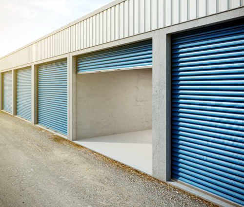 Storage units with blue doors, one open, along a gravel drive.