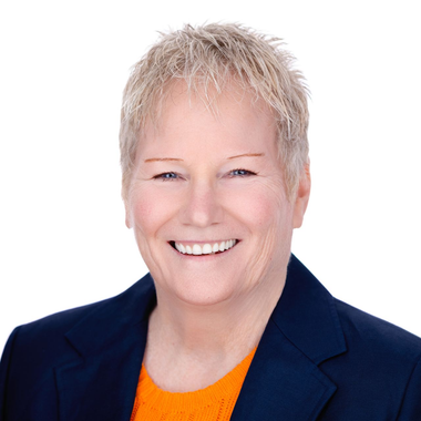 Smiling person in a navy blazer and orange top against a white background
