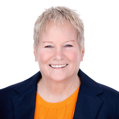 Smiling person in a navy blazer and orange top on a white background