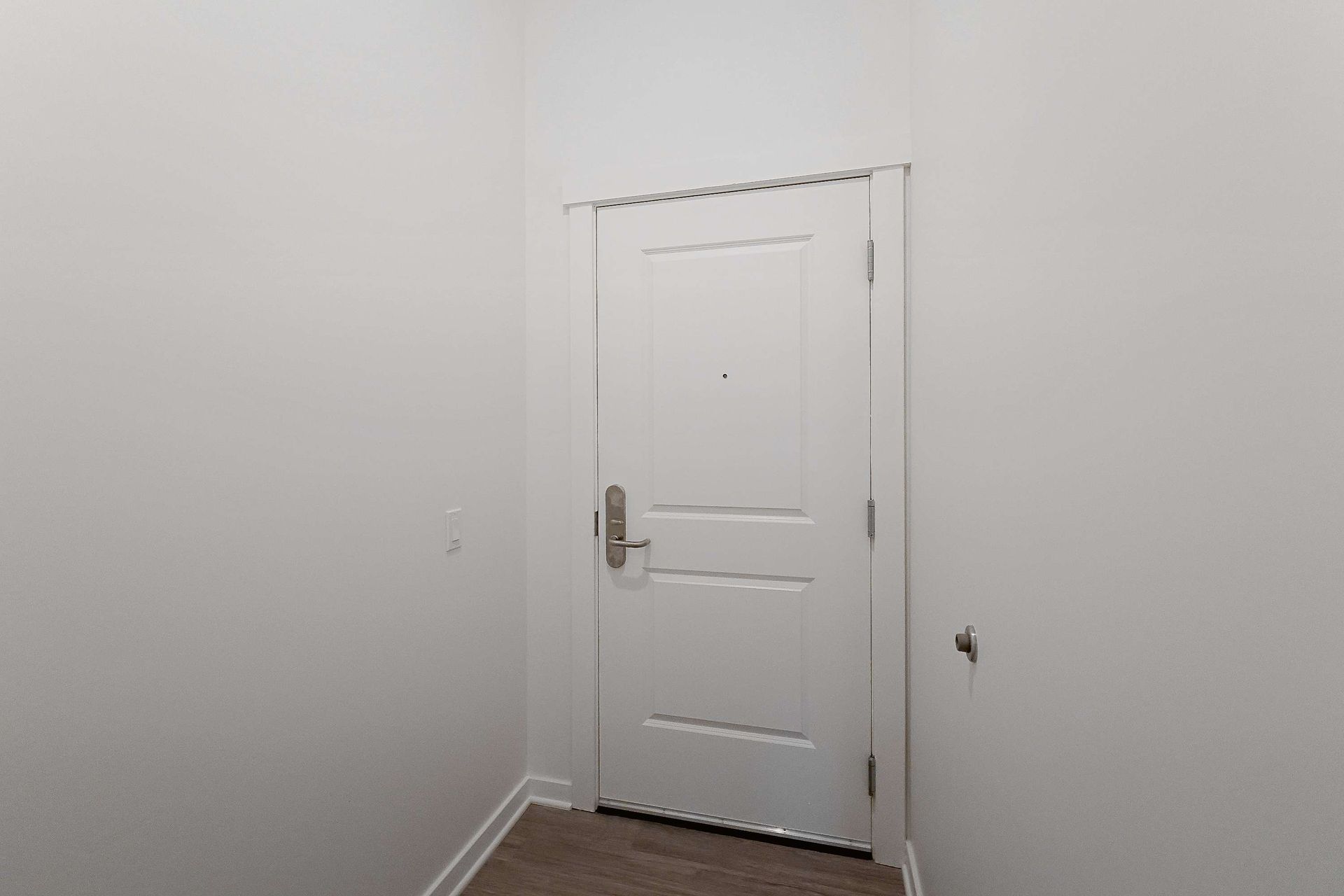 An empty hallway with a white door and a wooden floor.
