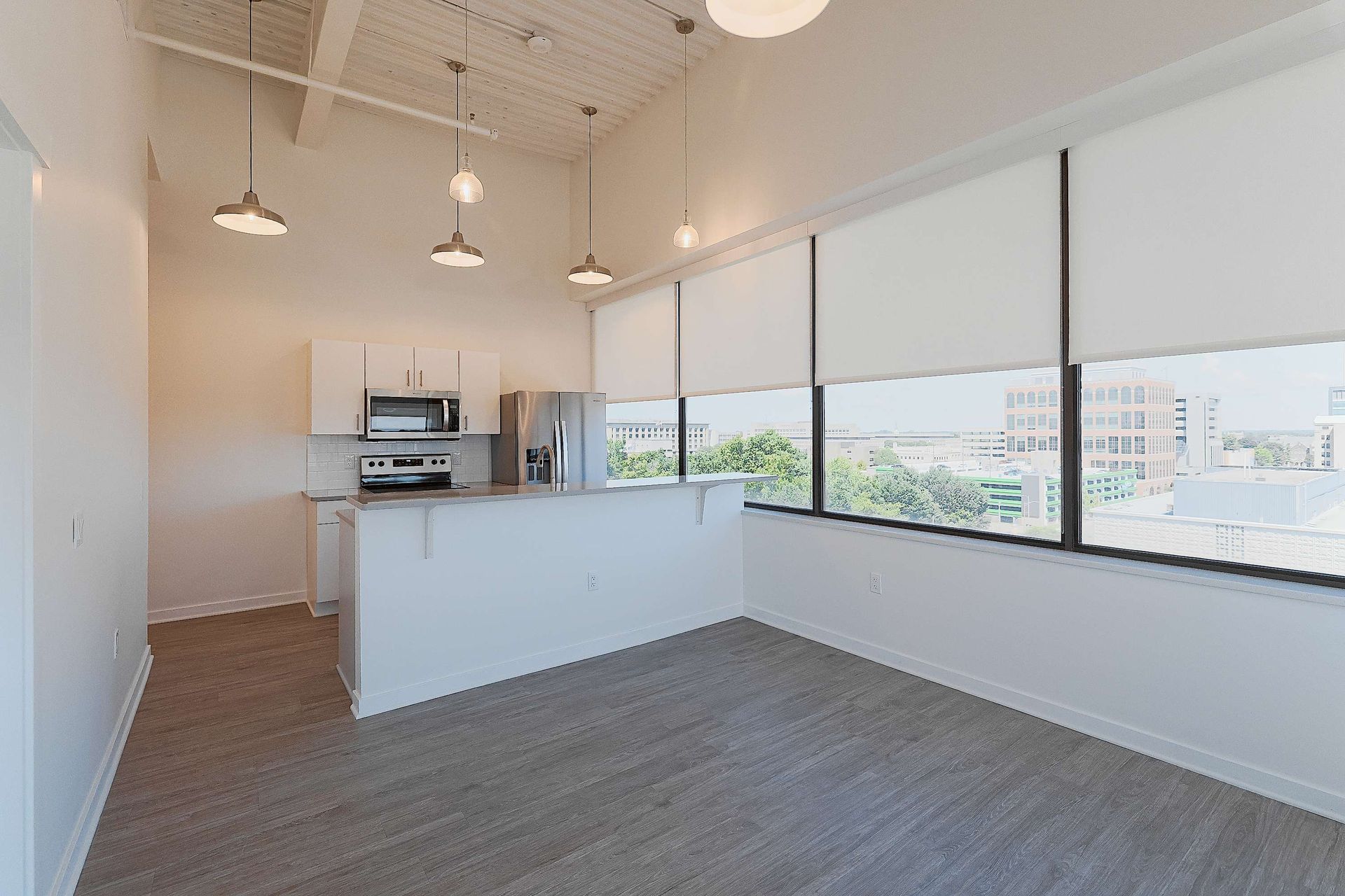 An empty apartment with a kitchen and a large window.