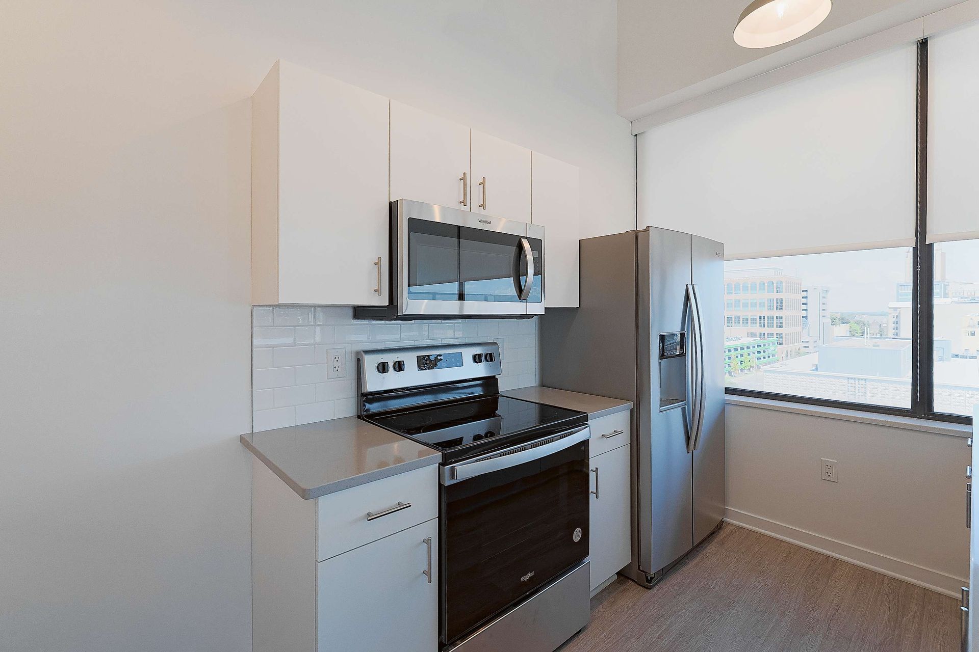 A kitchen with a stove , refrigerator , microwave and window.