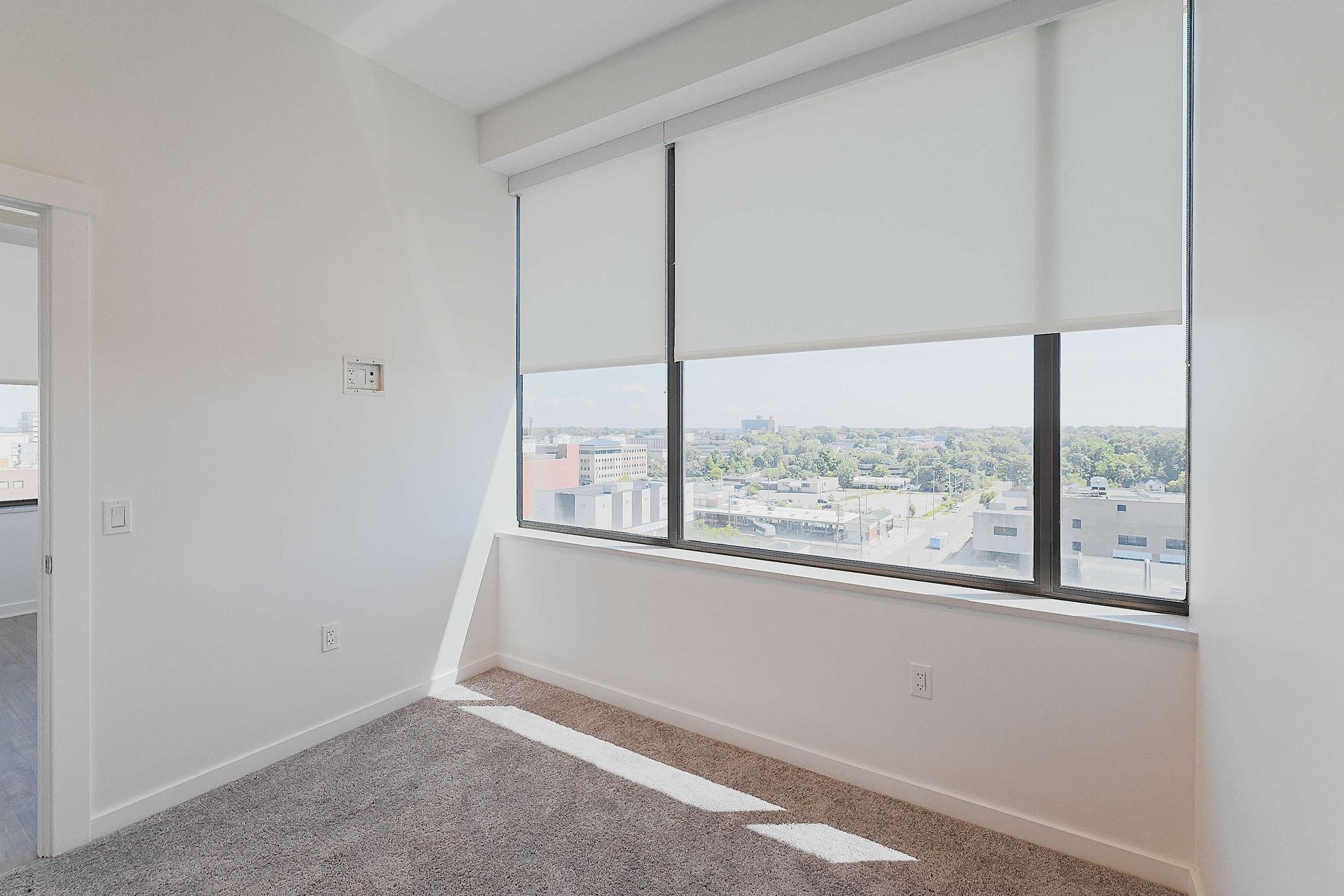 An empty bedroom with a large window and roller shades.