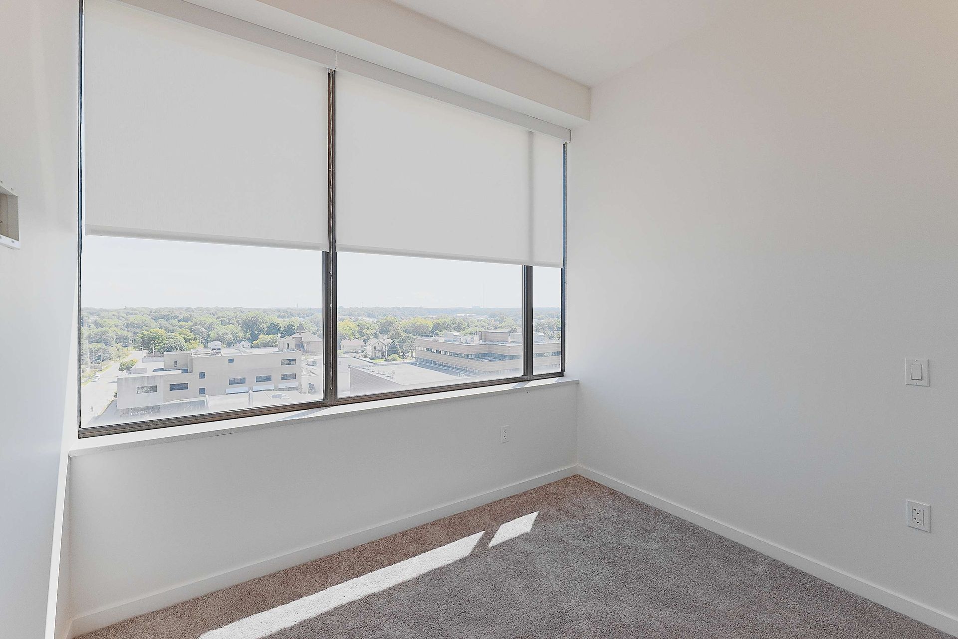 An empty bedroom with a large window and roller shades.