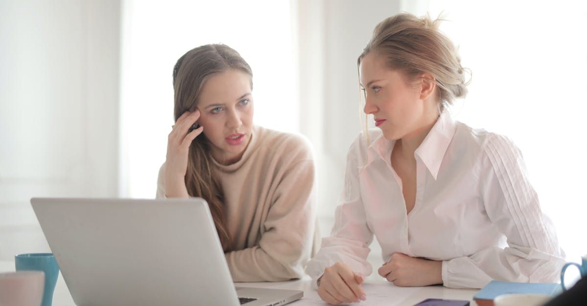 Two women, one with hand to forehead, looking at a laptop in a bright room.