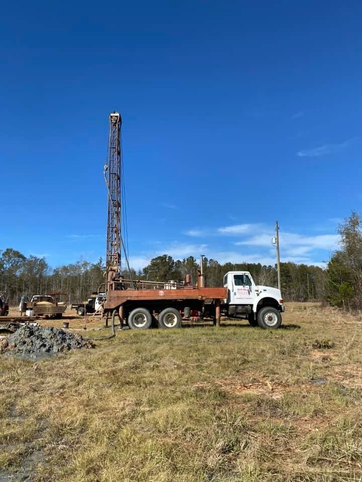 A well drilling truck in a grassy field under a blue sky.