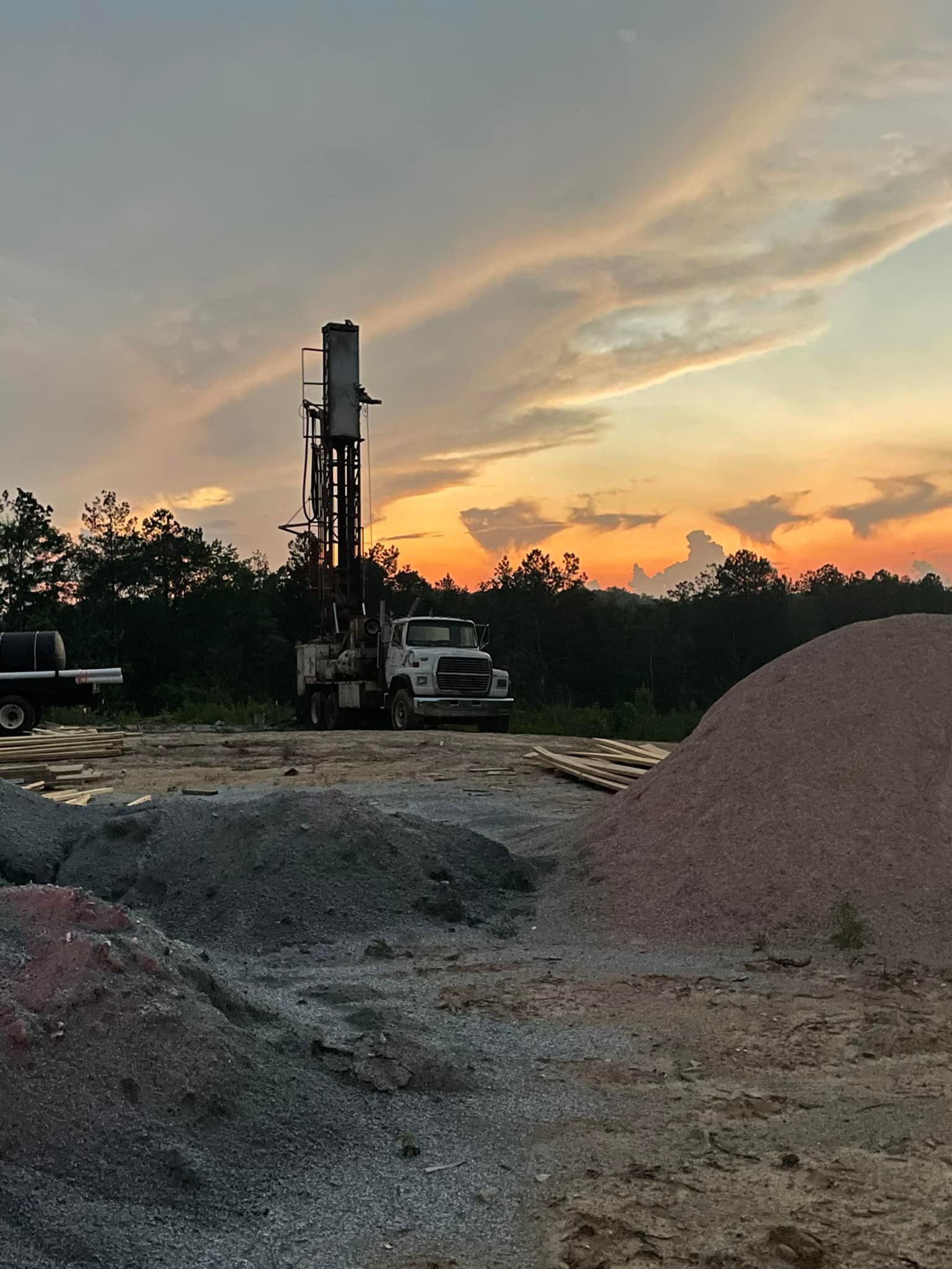 Drilling rig at sunset; piles of gravel in foreground.