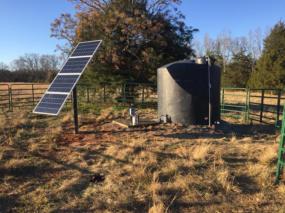 Solar panel next to a water tank in a field, fenced in.