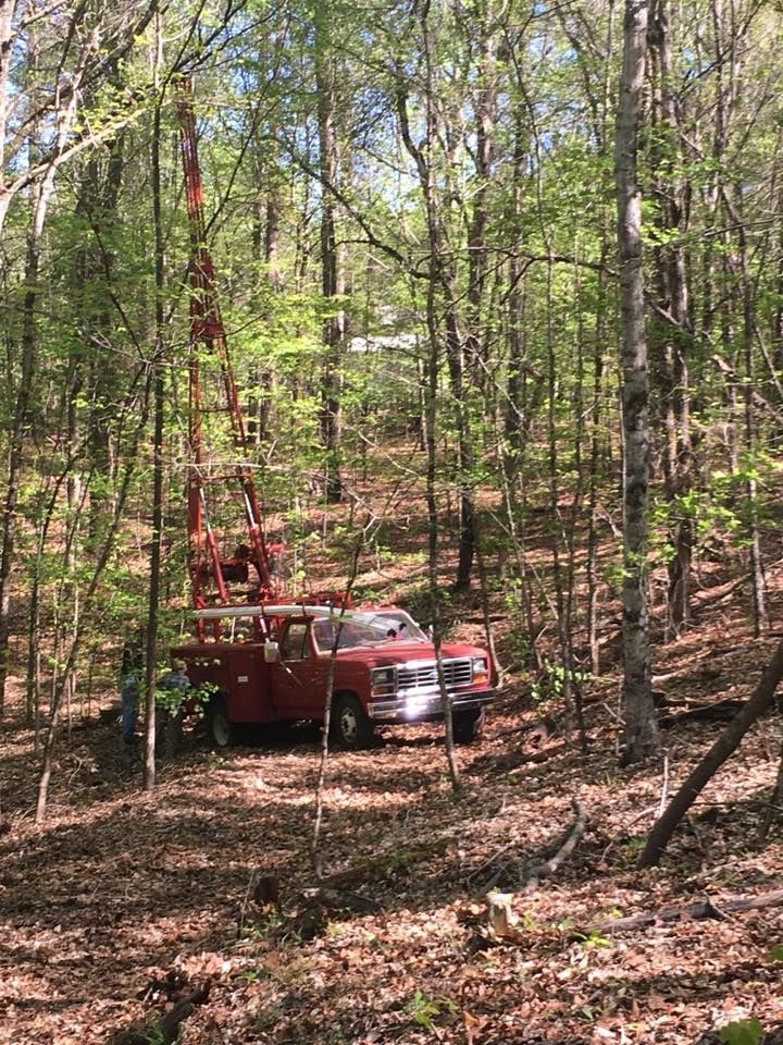 Red truck with crane in a wooded area, likely drilling.
