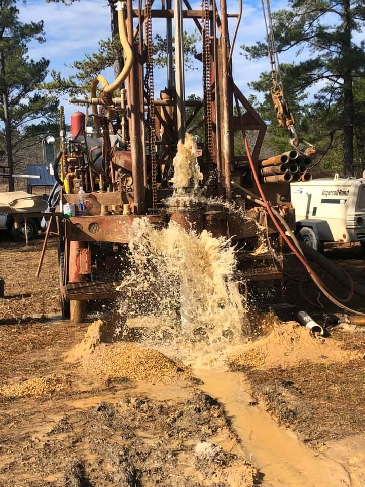 Drilling rig spewing muddy water, in an outdoor field setting.