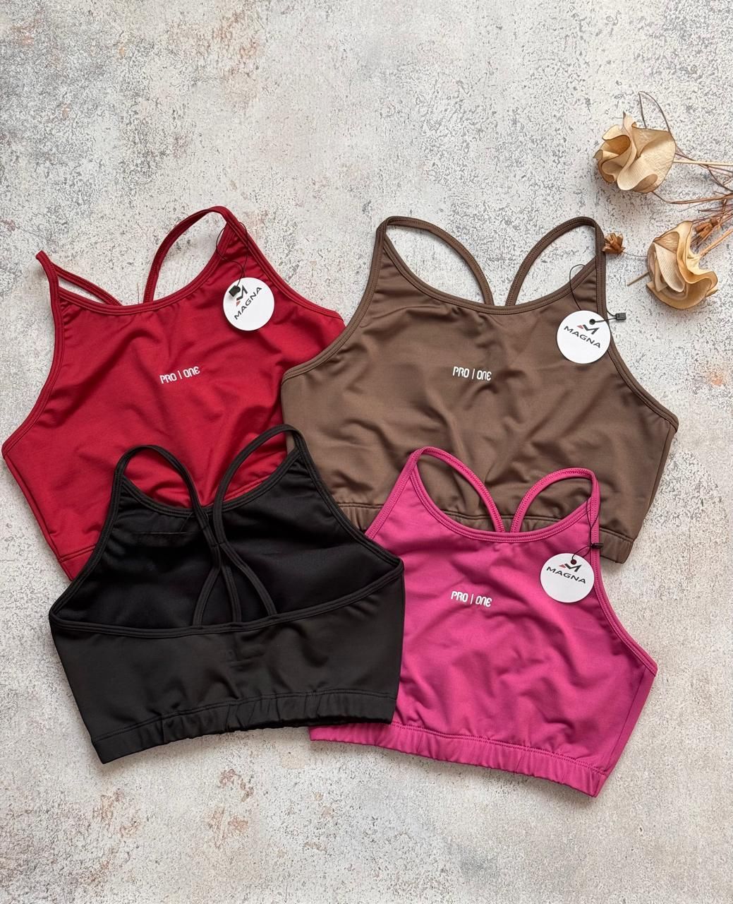 Cuatro sujetadores deportivos de mujer en rojo, marrón, negro y rosa sobre una superficie clara con textura.