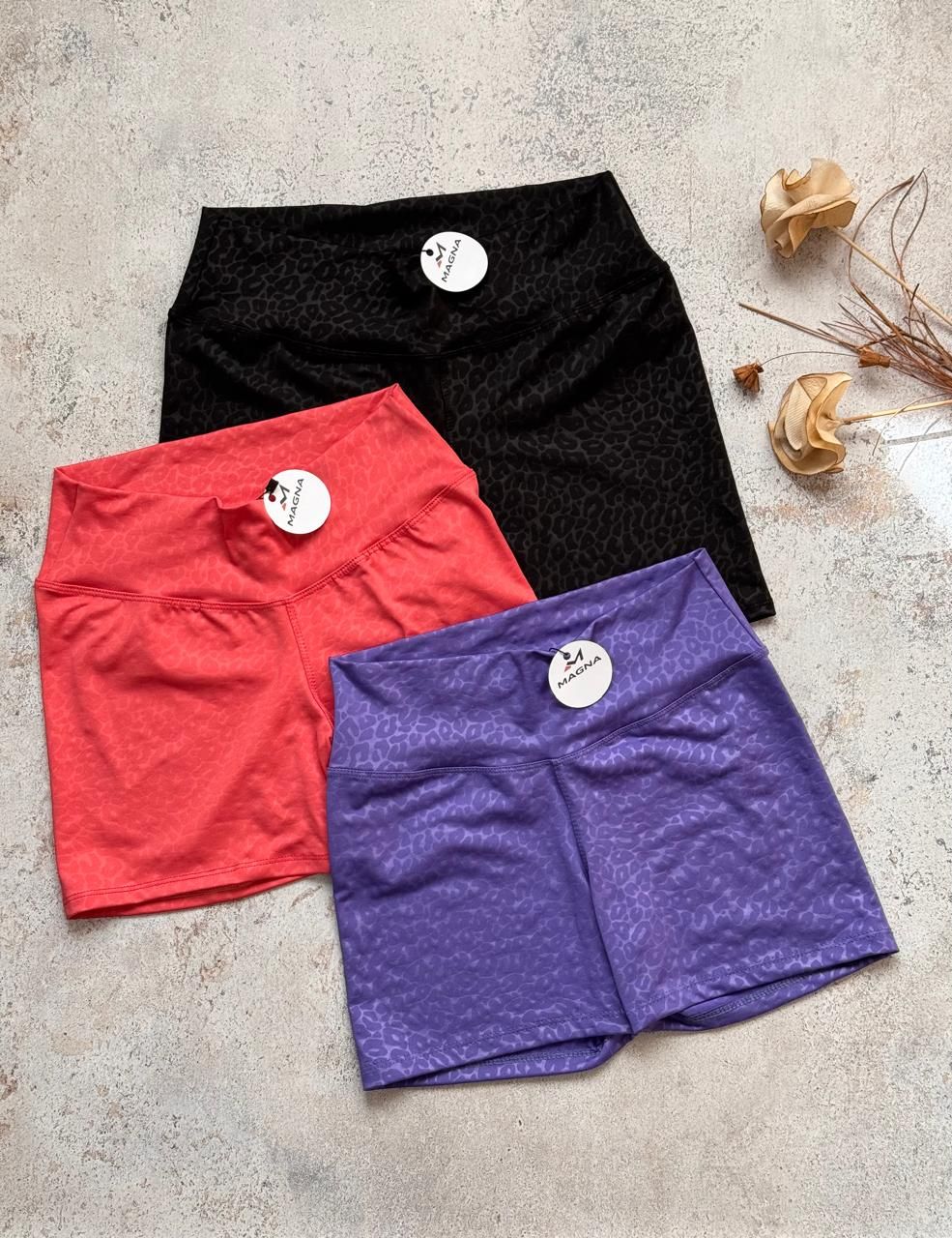 Tres pantalones cortos de mujer en negro, rojo y morado sobre una superficie clara, cada uno con una etiqueta colgante.