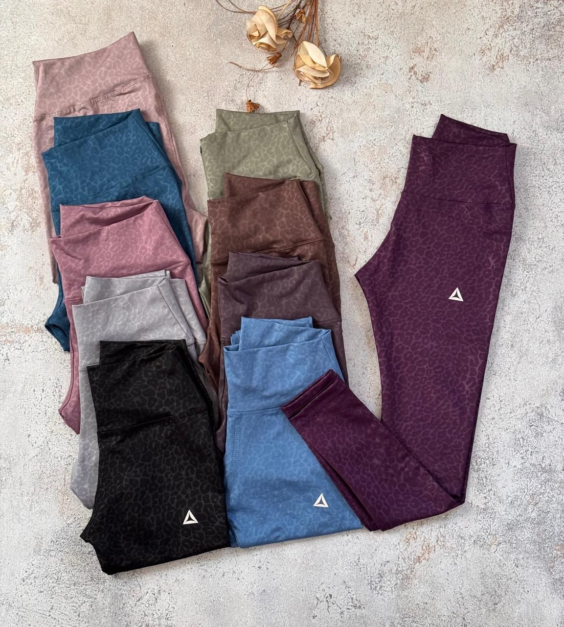 Leggings doblados y apilados en rosa, azul, gris, negro, verde oliva, marrón y morado sobre una superficie clara